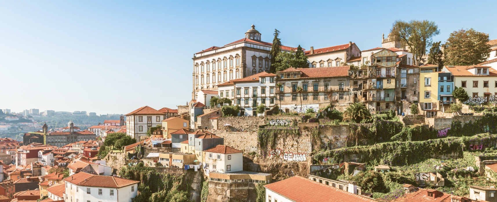 Scenic hillside view of Porto, Portugal, featuring terracotta rooftops, colorful historic buildings, and a grand stone structure overlooking the Douro River
