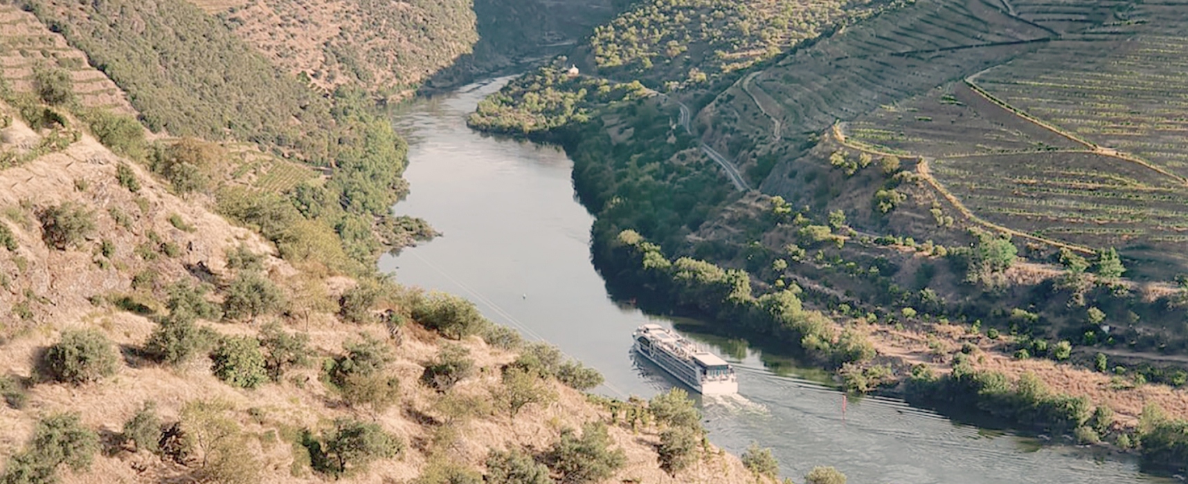 River cruise boat sailing through the winding Douro Valley in Portugal, surrounded by terraced vineyards and rugged hillsides.