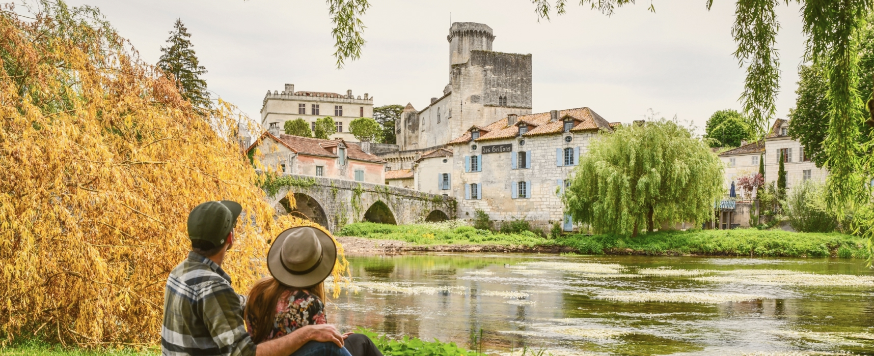 Couple sitting by a river and admiring bridge and castle in Bourdeilles