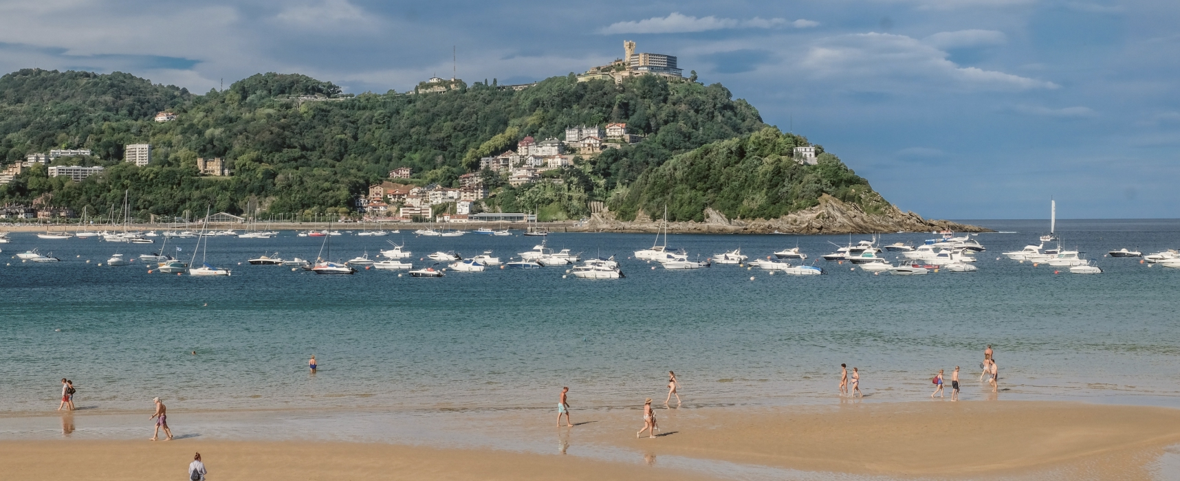 San Sebastian Beach with boats in the water and people walking in the sand
